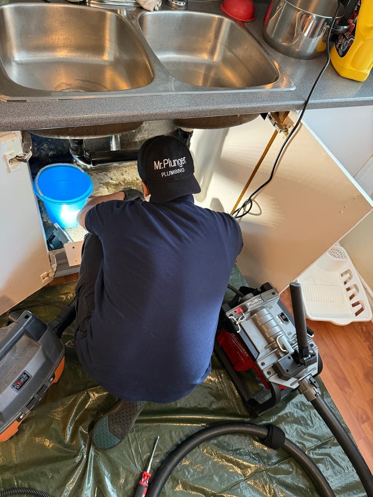 Mr. Plunger plumber clearing a kitchen sink drain with a powered auger